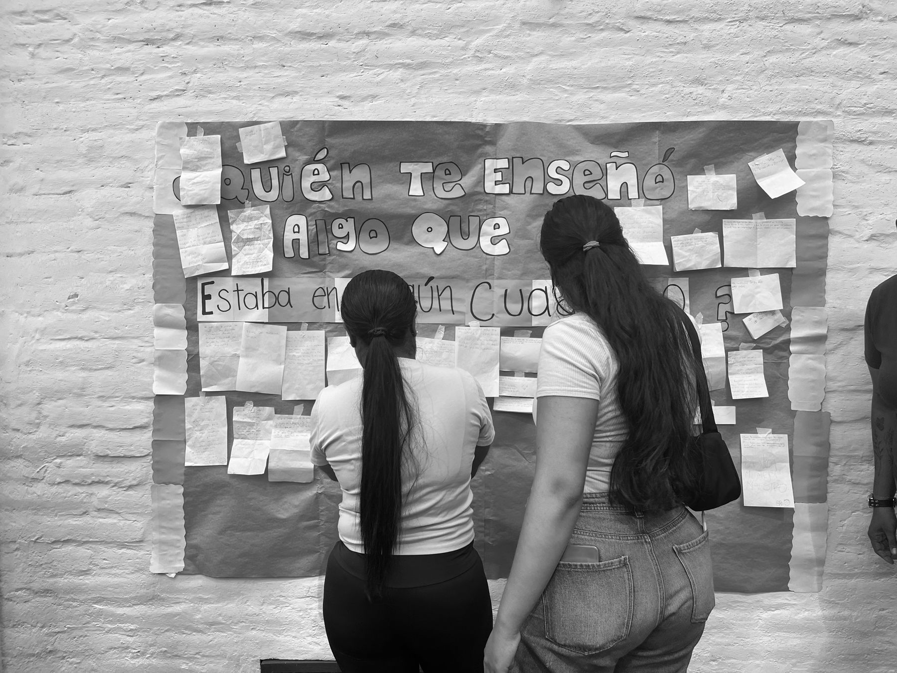 Dos estudiantes de espaldas leen las notas pegadas en un mural