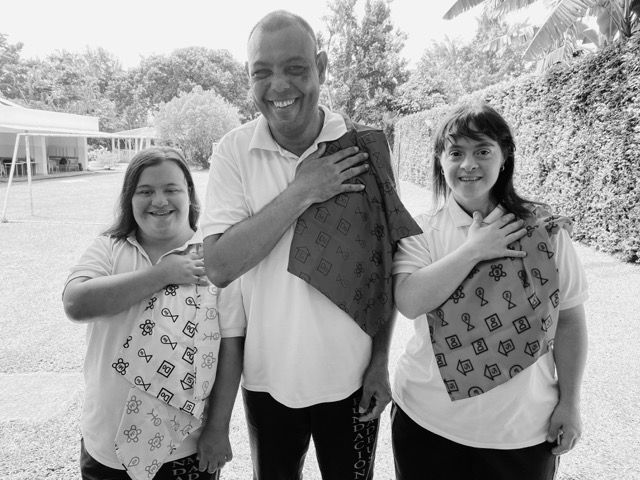 Tres estudiantes de la Fundación Amadeus sonríen con la mano en el pecho, sosteniendo pañuelos estampados