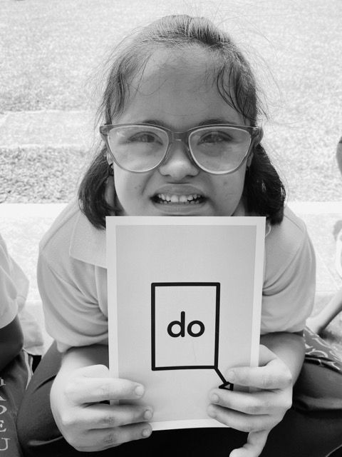 Una estudiante sonriente con gafas sostiene una tarjeta con la nota musical Do
